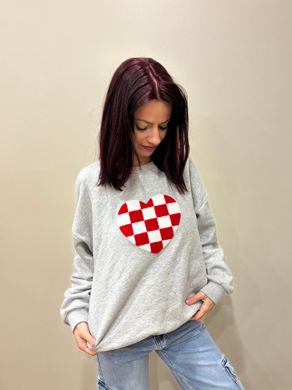 Person wearing a gray sweatshirt with a red and white pattern on a beige background